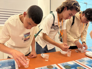 Jóvenes estudiantes en una mesa con muestras de polímeros en un vasos pequeños.