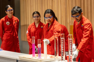 Estudiantes con batas color naranja experimentando con varios liquidos en probetas