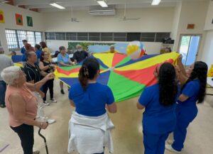 Adultos mayores participando de un ejercicio con mantel de colores y una bola.