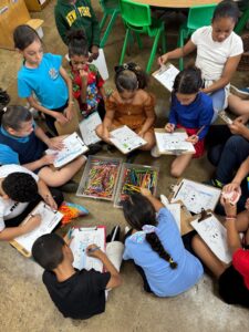 grupo de niños con libros para colorear compartiendo una caja repleta de crayones de diferentes colores.