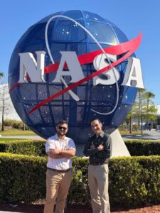 Dr. David Suleiman Rosado y Juan Camilo Rivera Díaz posando frente al logo esferico de la NASA.