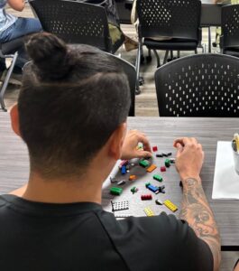 Estudiante en una mesa ensamblando un objeto con piezas de Lego.